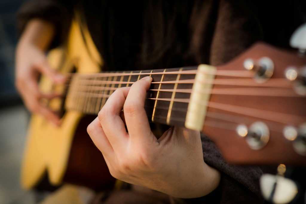 close-up of a man's fingers pressing down on the strings of an acoustic guitar