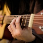 close-up of a man's fingers pressing down on the strings of an acoustic guitar
