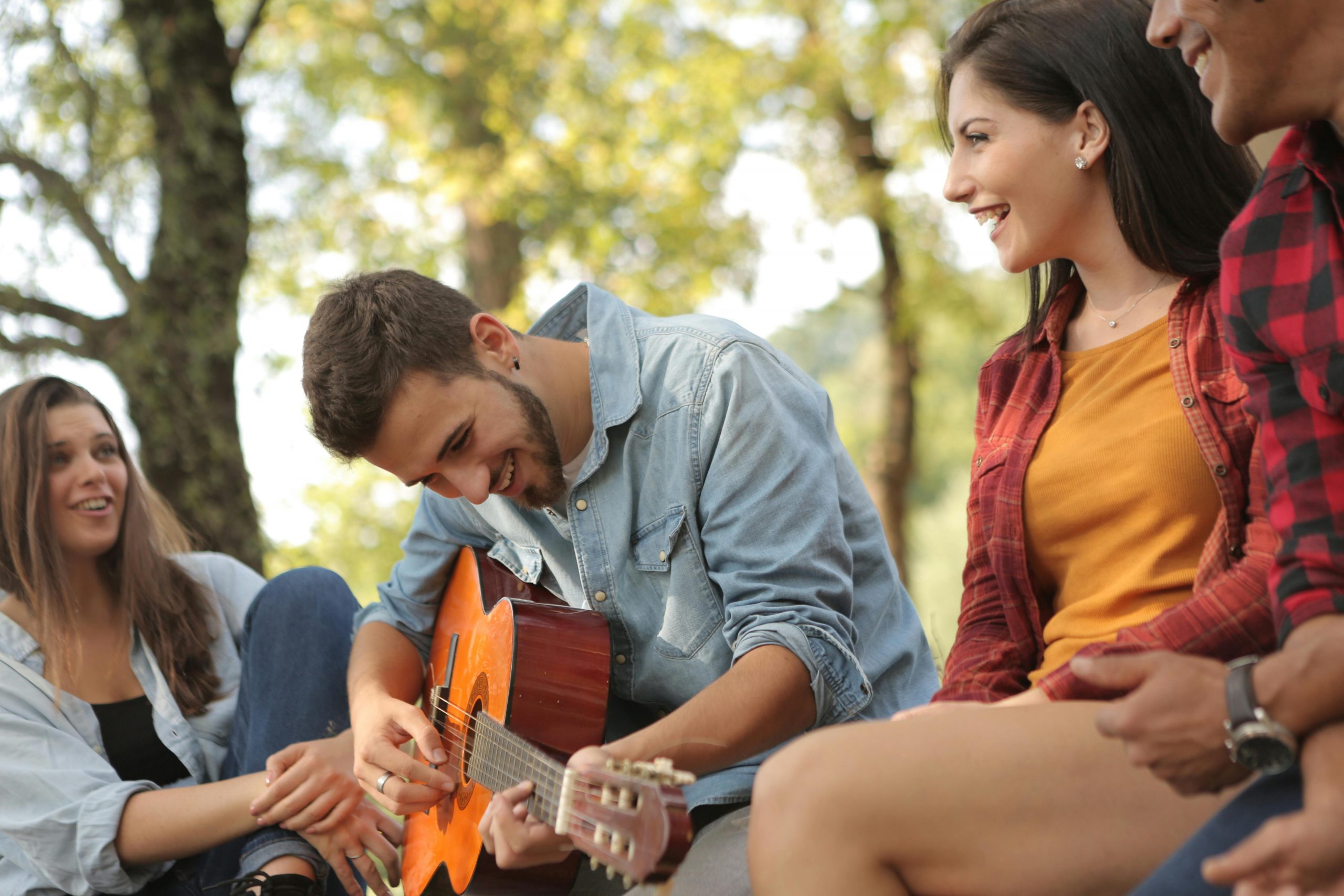 man playing a guitar outdoors while his friends are happily watching him